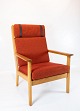 En høj lænestol 
i eg og rødt 
uldstof, 
designet af den 
legendariske 
danske 
møbelarkitekt 
Hans J. ...