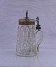 Drikkekrus med 
vippelåg, på 
toppen af låget 
står der en 
madonna. 
Glasset er med 
facetslibninger.
 ...