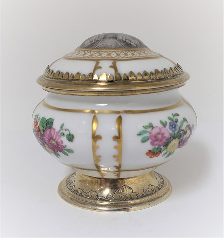 Royal Copenhagen. Bonbonniere af porcelæn, låg med motiv fra Kastellet, 
Kongeporten. Montering af forgyldt sterlingsølv, A. Michelsen, København 1921. 
H. 9 cm.