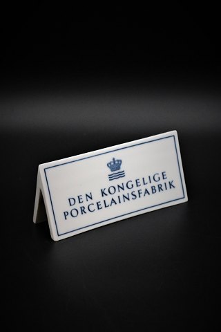 Gammelt forhandler skilt i porcelæn fra Royal Copenhagen 
"Den Kongelige Porcelænsfabrik" H:6cm. L:14cm.