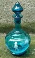 Blue decanter 
with stopper. 
Decorated with 
white enamel 
decoration of 
playful boy. 
Made in ...