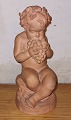 Terracotta 
figur 
forestillende 
putti siddende 
på en sten 
spisende druer 
fra drueklase. 
Små skår ...