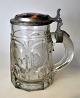 Tysk ølkrus i 
glas med 
tin/porcelæns 
låg, 19. årh. 
Presset 
glaskrus. Låg 
af tin og 
håndbemalet ...