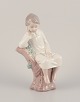 Lladro, 
Spanien. 
Porcelænsfigur 
af pige 
siddende på 
træstub. 
Ca. 1980.
Stemplet.
Perfekt ...