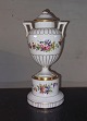 Urne vase pokal 
med låg i 
porcelæn 
stående på 
sokkel. Bemalet 
med blomster. 
Fremstillet på 
den ...