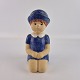 Keramikfigur af en hånddekoreret siddende pige med blå hat og kjole. Figuren hedder Dressed for ...