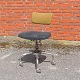 Ældre 
kontorstol hvor 
sæde og ryglæn 
er betrukket i 
koksgrå og 
grønlig stof og 
stel af metal. 
...