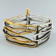 Anette Kræn; 
Bredt armbånd i 
sølv, delvist 
forgyldt. 
Monteret med 
skrue-splitlås. 
L. 18,6 cm. B. 
...