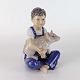 Figur i 
porcelæn med 
motiv af en 
lille gris i 
armene på en 
siddende dreng. 
Nr. 735
Producent ...