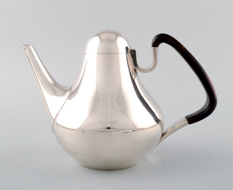 Georg Jensen, nummer 1017. Kaffekande med håndtag af guajaktræ.
Vægt 670 gram. 
Tegnet af Henning Koppel (1918-1981) år 1952.